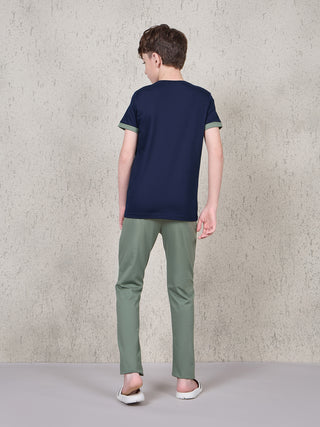 BOYS standing, wearing a navy blue t-shirt with olive green sleeves and olive green pants.
