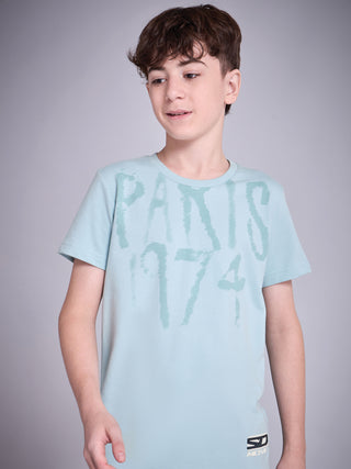 Boy standing in a slight side pose wearing an ice blue short-sleeve T-shirt with tonal “PARIS 1974” typography print and SD Move logo detail.