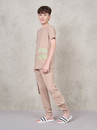 Boy standing in a side pose wearing a beige short-sleeve pyjama set with matching full-length jogger pants and neon green SD graphic print.