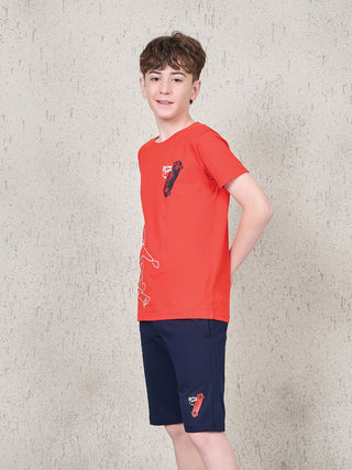 Boy standing in a side pose wearing a ferry red short-sleeve T-shirt and navy shorts sleepwear set with skateboard graphic print.