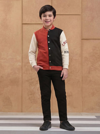 BOYS in a studio shot, wearing a red, black, and cream color-blocked bomber jacket with graphic print, and black pants.