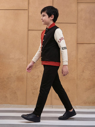Boys walking in a varsity jacket with black, red, and cream panels, black pants, and black sneakers.