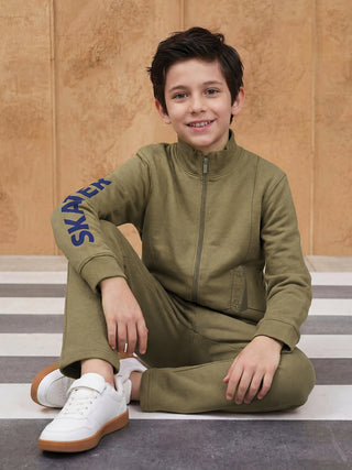 BOYS in a seated pose wearing a khaki green tracksuit with "SKATER" printed on the sleeve and a skateboard graphic on the leg.