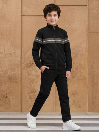 A young boy is posing in a black tracksuit with grey and yellow stripes.