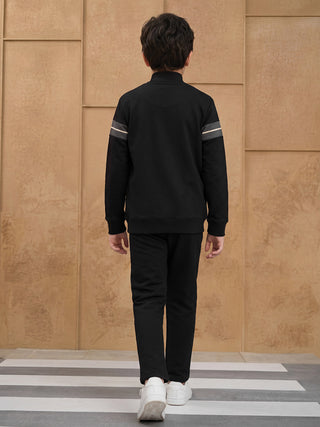 BOYS walking away from camera wearing black tracksuit with white striped sleeves and white sneakers.