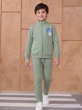 A young boy in a green tracksuit walks forward, smiling.