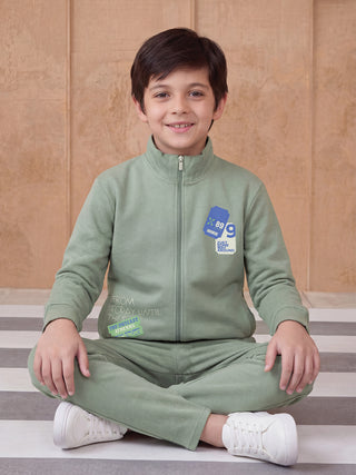 Boys in a green sweat suit with print detail, sitting cross-legged.