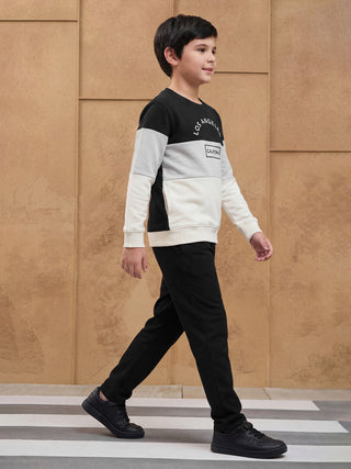 BOYS walking on a crosswalk wearing a black, grey, and cream colorblock sweatshirt with "Los Angeles" and "California" print and black pants.