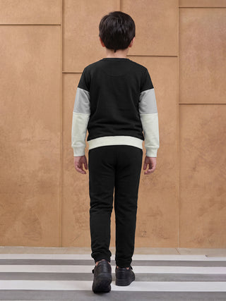 BOYS wearing a black, gray, and white color-blocked sweatshirt with black pants, standing from the back.