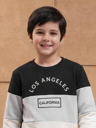 A young boy in a black and grey color-blocked sweatshirt with "LOS ANGELES" and "CALIFORNIA" printed on it.