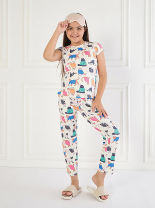A young girl in a white pajama set with a colorful cat print and a pink sleep mask on her head poses playfully against a white background.