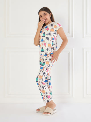 A young girl in white pajamas with a colorful cat print poses playfully.