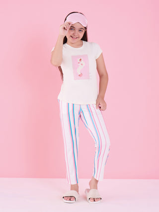 A young girl in a pink sleep mask, white t-shirt with a pink graphic, and pink and blue striped pajamas stands on a pink background.