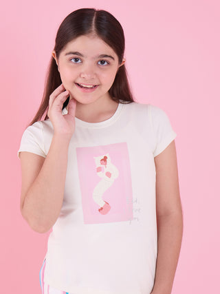A young girl smiles and poses in a white pajama top with a graphic print of a person sleeping in bed and the text "Bed, I love you,".