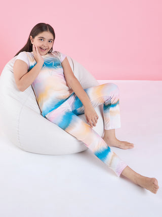 A young girl with a tie-dye pajama set featuring a star design sits comfortably on a beanbag.