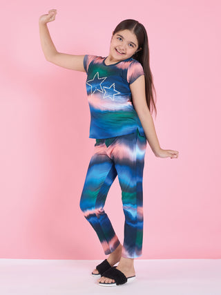 A young girl poses with one arm raised, wearing a tie-dye sleep set with star prints.