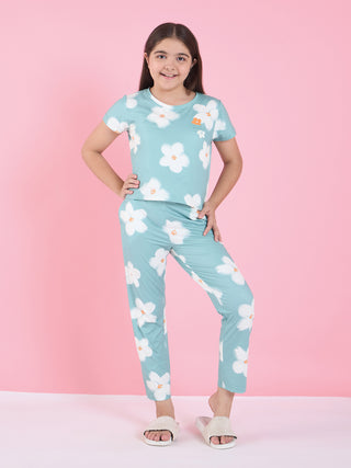 A young girl models a light blue pajama set with white floral print, featuring a short-sleeved top and long pants.