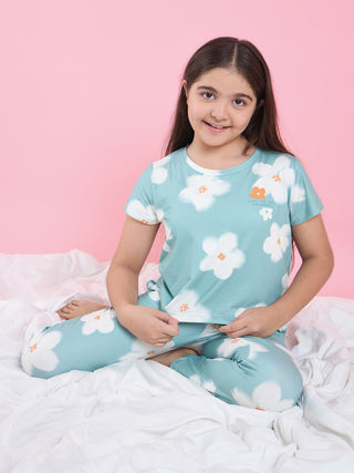 A young girl with long dark hair sits cross-legged on a white duvet, wearing a light blue pajama set with a white floral print and the words "LIVE FOR THE MOVEMENT" on the shirt.
