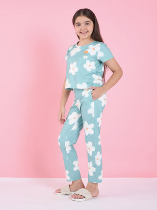 A young girl stands with her hand in her pocket, wearing a light blue pajama set with a white floral print.