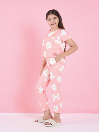 A young girl in a pink pajama set with a floral print, wearing white fuzzy slippers and posing with her hand in her pocket.