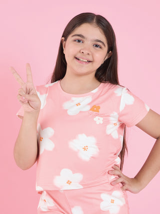 GIRLS wearing a pink pajama set with a floral print, with one hand on her hip and the other making a peace sign.