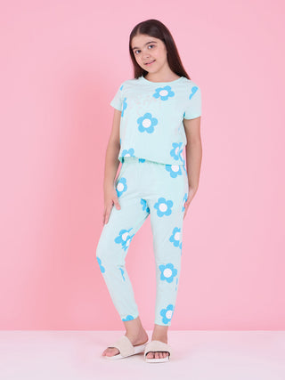 A young girl in a mint green pajama set with a blue floral print, posing standing with her hands at her sides.