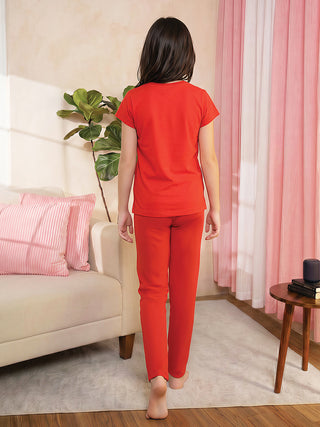 A young girl walks away from the camera wearing a red short-sleeved t-shirt and red pajama pants.
