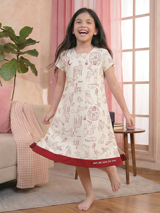A young girl in a cream-colored sleep dress with a playful dog print and a red hem smiles joyfully.