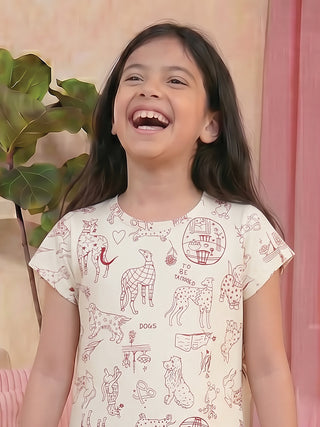 A young girl with long, dark hair laughs joyfully while wearing a cream-colored short-sleeved sleep shirt with a playful all-over print of various dog breeds in a dark red line art style, and a whimsical circular graphic that says "TO BE TATTOOED".