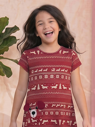 A smiling young girl in a red Christmas-themed pajama dress with a dog appliqué.