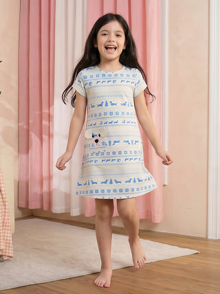 A young girl in a light blue and white dog-print sleep dress with a smiling dog face applique stands with her legs apart and arms outstretched.