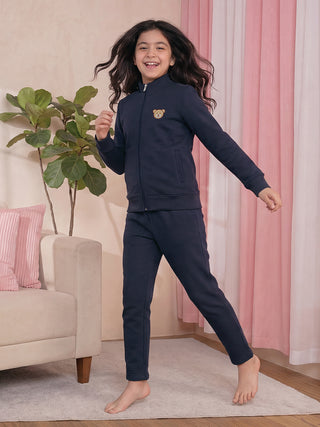 A young girl in a navy blue pajama set with a teddy bear print is jumping in the air, smiling.