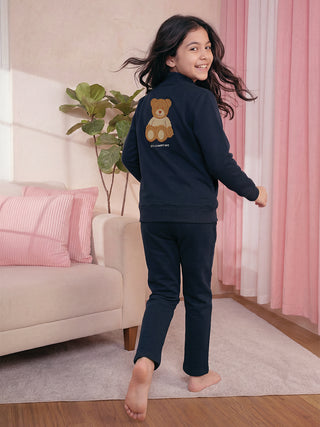 A young girl in navy blue pajamas with a teddy bear print on the back, posing playfully.