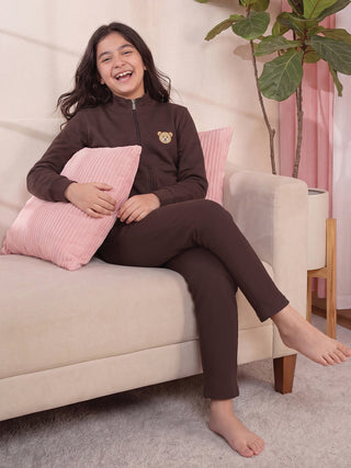 Girls wearing a brown ribbed pajama set with a teddy bear print, posing on a sofa with a pink pillow.