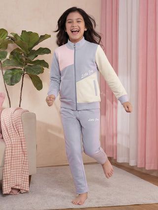 A young girl in a color-blocked light purple and pale pink tracksuit with "Little Joy" printed on it is jumping.