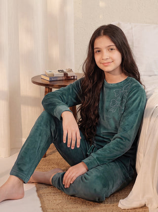 Girls in teal velvet pajamas with a subtle butterfly print, sitting on the floor next to a bed.