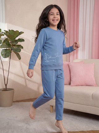 A young girl with long, dark hair smiles broadly while wearing a blue sweatshirt with a white dachshund print and matching blue sweatpants.