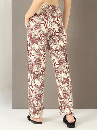 Women's cream and brown leaf-print wide-leg pajama pants, worn from behind with a hand in the pocket.