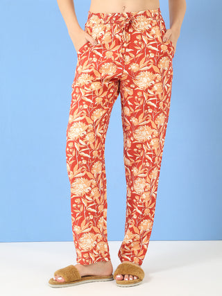 Women posing with their hands in the pockets of red floral print pajama pants.