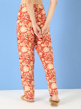 Women posing with hands clasped behind their back, wearing loose-fitting, rust-colored floral print pajamas.