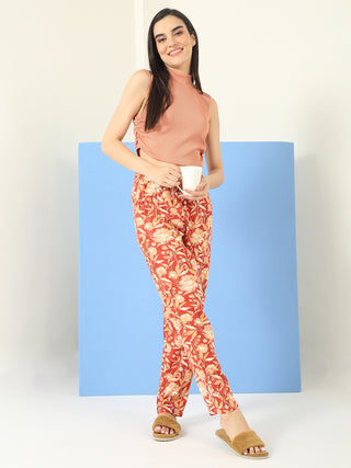 A woman poses in a coral ribbed knit sleeveless top and red floral print pants, holding a white mug.