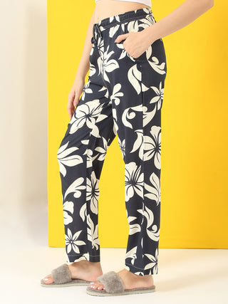 Women in a relaxed pose, wearing navy blue floral print pajama pants and grey fuzzy slippers.
