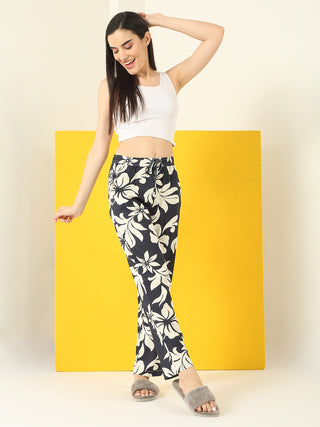 A woman poses in a white tank top and black floral print sleep pants.