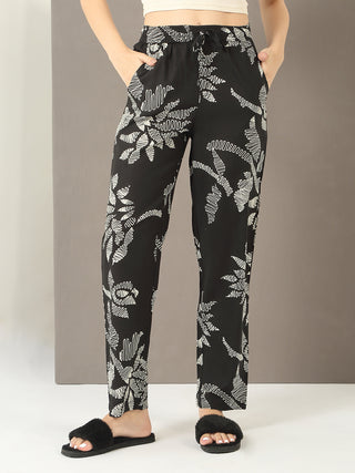 Women wearing black pajama pants with a white tropical leaf print and furry black slides.