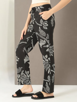 Women's black pajama pants with a white abstract floral print, styled with fuzzy slippers.