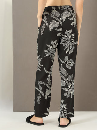 Women in a standing pose wearing black floral print pajama pants.