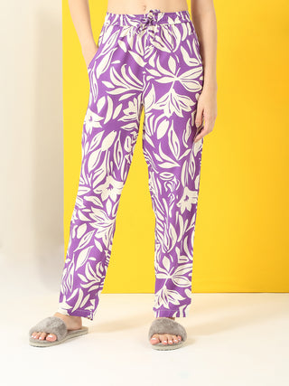 Women wearing purple floral print pajama pants and gray slippers, standing with hands in pockets.