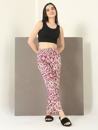 A woman stands in a relaxed pose wearing a black cropped tank top and patterned maroon pajama pants.