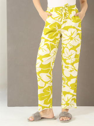 Women's lime green floral print pajama pants with a drawstring waist, posed with hands in pockets and wearing fuzzy slippers.