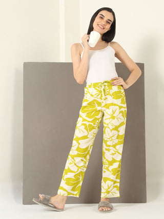 Women in a relaxed pose wear a white tank top and yellow floral print pajama pants, holding a mug.